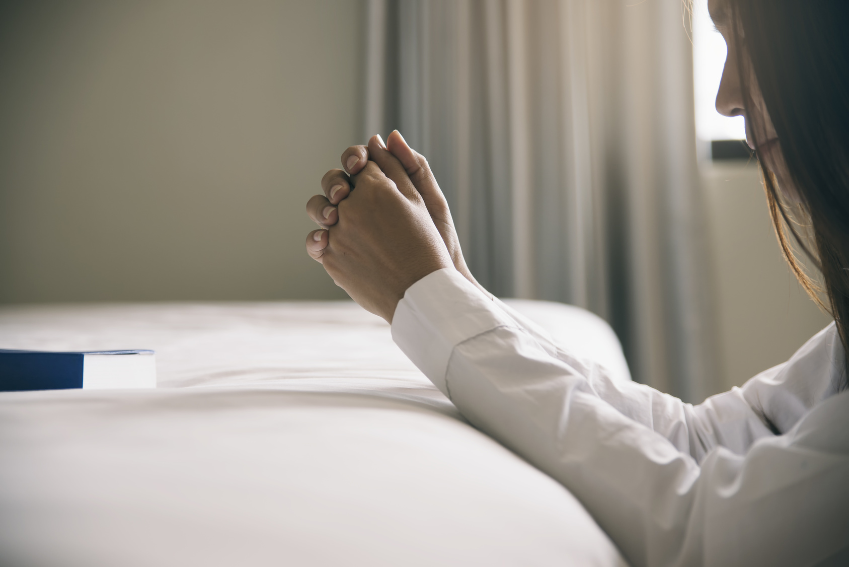 Beautiful woman (christian) hands on bible,thinking and closed her eyes at bed room.Person side view,Asian female praying by hand in hand together,hope for peace and read bible.Pray and bible concept.